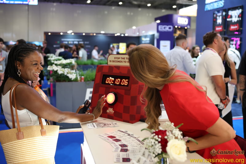 Event attendee interacting with a booth hostess at iGB L!VE London 2026, photographed by CasinoLove